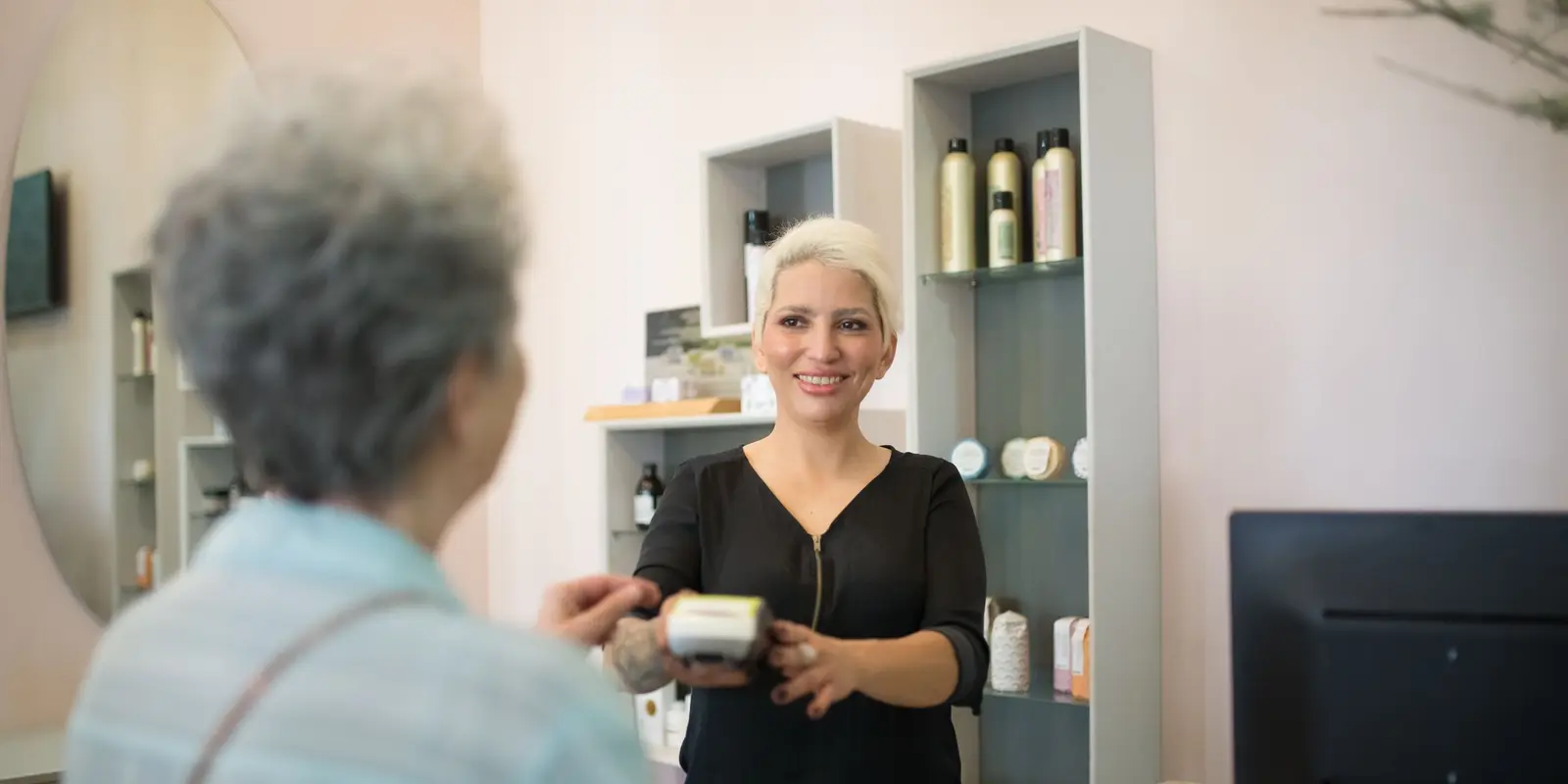 Salon owner smiling behind her front desk as she hands a client the card reader